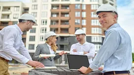 A group of construction professionals in safety helmets collaborating on-site with plans and a laptop, representing advanced Construction Management QLS Level 7.