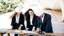 Three construction professionals in safety helmets reviewing project plans outdoors, illustrating introductory skills for Construction Management QLS Level 1 Award.