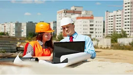 Two construction professionals reviewing site plans on a laptop at an active project location, representing advanced skills in Construction Site Management QLS Level 5.