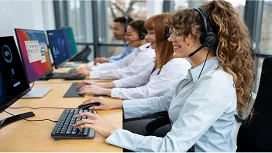 Customer service representatives wearing headsets work at desktop computers, showcasing teamwork and communication skills in customer service training.