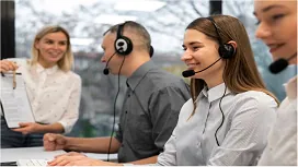 Customer service representatives wearing headsets work at their desks while a supervisor provides guidance, illustrating advanced customer service training.