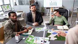 Team of professionals reviewing environmental maps and renewable-energy models during a planning session for Level 3 environmental management training.