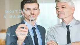 Two professionals reviewing a written strategy on a glass board, symbolizing emotional intelligence and leadership enhanced through AI-driven insights.