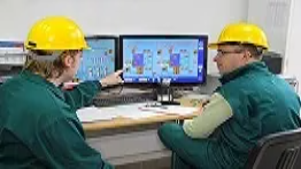 Two facility technicians in safety helmets monitoring building systems on dual computer screens, representing core skills in facilities management.