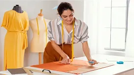 A fashion design student cutting fabric on a worktable with mannequins in the background, representing hands-on training in Fashion Design Level 3.