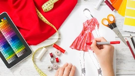 Hands sketching a red dress surrounded by fabric, colour swatches, sewing tools and a tablet, representing essential fashion design skills