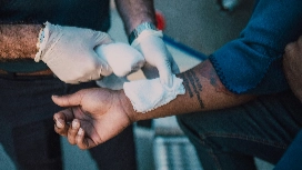 Gloved hands applying a bandage during first aid training – learn essential first aid skills online with OHSC