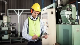 Employee wearing safety equipment reviewing workplace information in an industrial setting – learn flexible working skills online