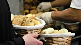 Gloved food worker handling fresh bread baskets, showing safe hygiene practices in OHSC Food Safety course
