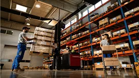Warehouse workers managing stock as a forklift lifts pallets, illustrating key skills in inventory control and supply chain operations.