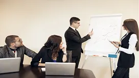 Team attending a business presentation where two professionals explain a workflow diagram, representing foundational skills in Level 2 leadership and management training.