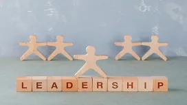 Wooden figures symbolizing teamwork with a central leader figure standing above blocks spelling “leadership,” representing Level 3 leadership training.