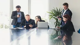 Team of office professionals collaborating around laptops and tablets, representing foundational teamwork and leadership skills taught in Level 1 management training.