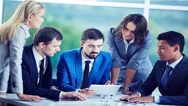 Professional team collaborating around a tablet during a meeting, representing advanced leadership, communication, and people management skills taught in Level 5 training.