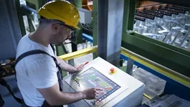Factory worker using a digital control panel to monitor production processes, illustrating lean management in manufacturing practices.
