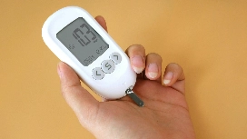 Hand holding a blood glucose monitor, representing basic patient care and monitoring skills taught in a Level 3 health and social care diploma.