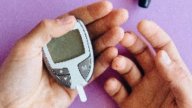 Hands using a blood glucose monitor, representing patient care awareness and management skills taught in a healthcare management course online Level 4.