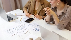 Accounting professionals reviewing financial reports with a calculator and laptop, illustrating analytical skills in accounting and finance training.