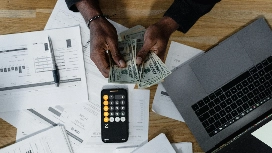 Finance professional reviewing reports and cash with calculator and laptop, representing level 7 diploma in accounting and finance