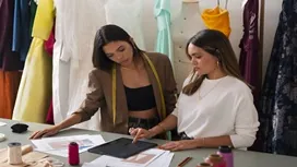 Two advanced fashion designers reviewing fabric samples and sketches in a professional studio, reflecting the expertise taught in the Level 7 Diploma in Fashion Design.