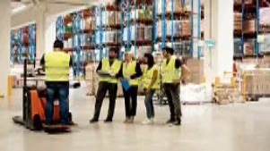 Warehouse staff in safety vests receiving operational guidance from a forklift operator, representing basic skills taught in Level 1 logistics management courses.