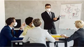Business professional presenting management strategies to a team wearing masks, representing core skills taught in Level 4 management and leadership training.