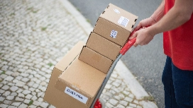 Worker transporting stacked cardboard boxes on a trolley, illustrating safe lifting techniques and essential manual handling practices in the workplace.