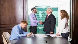 Business professionals in a meeting shake hands while others review documents, representing negotiation, communication, and conflict-resolution skills training.