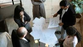 Team of professionals reviewing workflow diagrams together, representing coordination, planning and process optimisation in operations management courses.