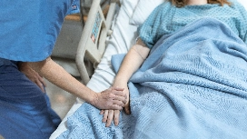 Healthcare worker providing bedside support and comfort to a patient, demonstrating essential patient care techniques