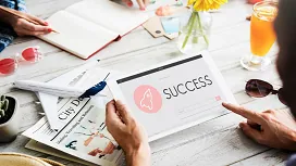 People collaborating around a table with a tablet displaying “Success,” symbolizing goal setting, growth, and advanced personal development at Level 7.