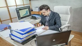 Man reviewing financial documents at a desk with files and a computer, representing personal income tax account management training.