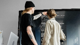 Two professionals reviewing content on a large screen, representing communication, visual clarity and delivery techniques taught in presentation skills courses.
