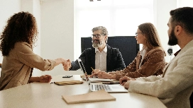 Job candidate shaking hands with interviewers in a meeting room, symbolizing effective interviewing, selection and recruitment skills in HR training.