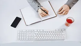 A person writing notes in a journal at a clean desk setup, representing online training for remote creative writing careers.