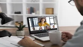 A remote worker participates in an online meeting on a laptop while preparing documents, representing training for remote data entry careers.