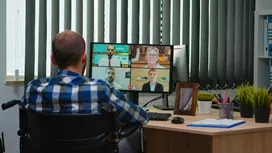 A remote manager participates in an online video conference with a team displayed on a monitor, representing training for remote management careers.