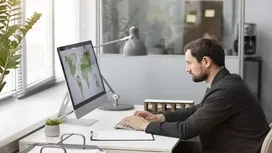A man working remotely on a desktop computer reviewing global project data, representing online remote project management careers.