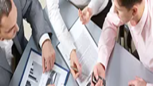 Business professionals reviewing documents and charts during a meeting, illustrating skills in writing reports and preparing proposals.