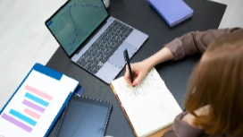 Student taking research notes beside laptop and charts, supporting OHSC Research Skills short course online.