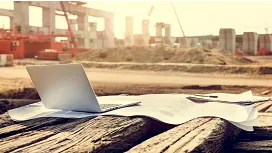 A laptop and construction blueprints on wooden beams at an active site, symbolizing essential planning and coordination skills for QLS Level 2 Site Management.