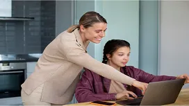 A teaching assistant guiding a student working on a laptop, illustrating supportive learning and classroom assistance taught in Level 3 teaching assistant courses.