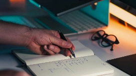 Person writing notes in a planner at a desk with a laptop, symbolizing organisation, scheduling and productivity skills taught in time management courses.