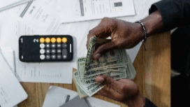 Hands counting cash beside calculator and invoices – learn debits and credits in accounting online with OHSC