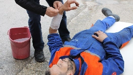 Workplace first aid responder bandaging an injured worker's arm during practical first aid and safety training